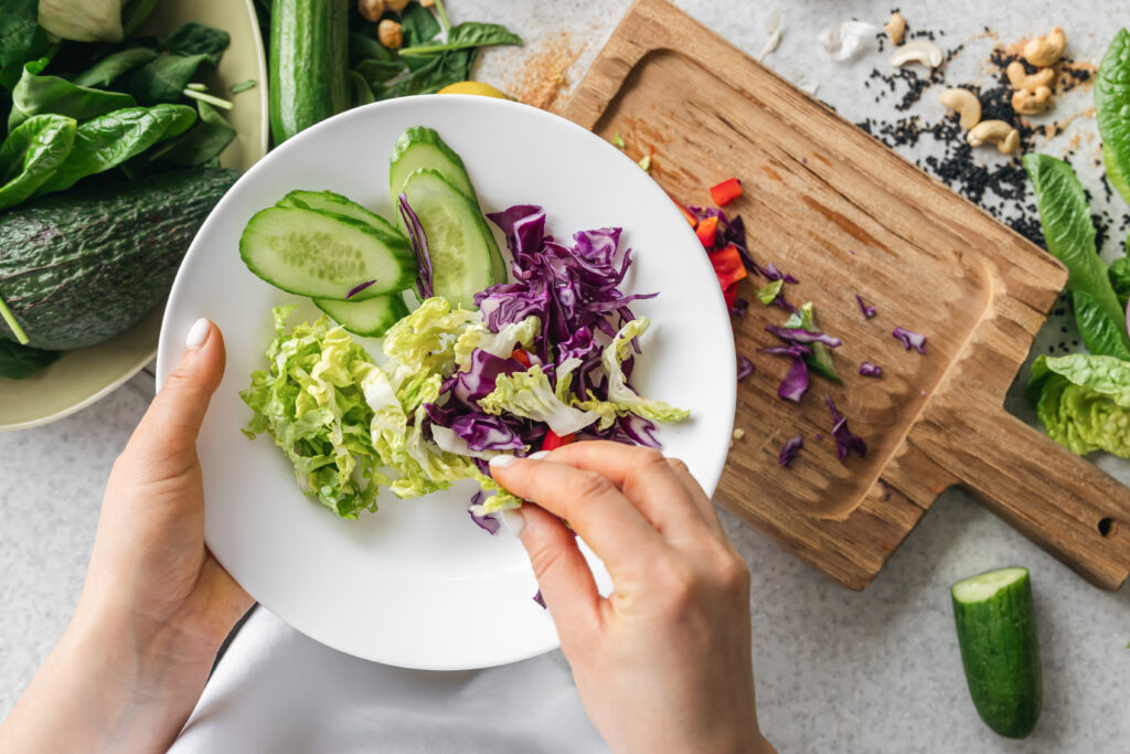 A plate with chopped fresh vegetables in female hands in the kitchen, top view.